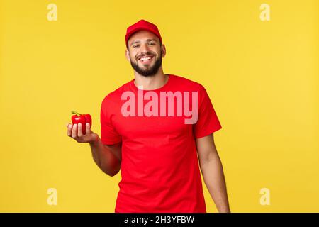Livraison en ligne, achat et concept de commande de nourriture.Beau coursier gai en casquette et t-shirt rouge uniforme, tenant le poivre frais Banque D'Images