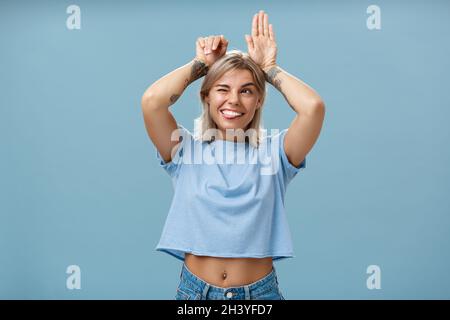 Photo en studio d'une femme charmante et insouciante et émouvante avec des tatouages sur les bras qui agissent comme un lapin avec des palmiers sur la tête W. Banque D'Images