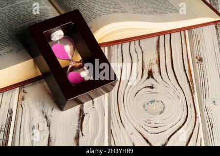 Verre de sable sur table en bois avec livre ouvert gros plan Banque D'Images