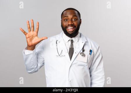Sympathique-regardant gai beau afro-américain médecin, homme médecin montrant cinq, cinquième chiffre avec la main, souriant heureux Banque D'Images