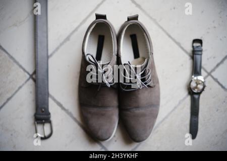 Chaussures, ceinture et montre-bracelet en daim gris Derby pour homme sur sol en pierre. Banque D'Images