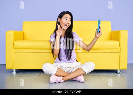 Une femme asiatique souriante vlogger enregistrant une vidéo sur un téléphone portable montrant le signe de la victoire. Banque D'Images