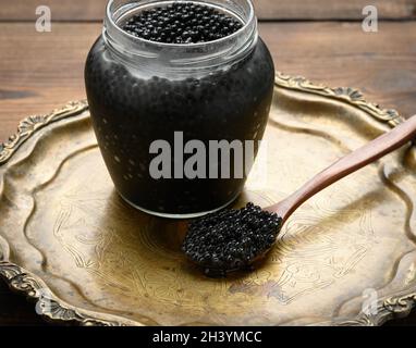 Caviar de paddlefish noir frais dans une cuillère en bois brun et une pleine canette de caviar sur une table en bois Banque D'Images