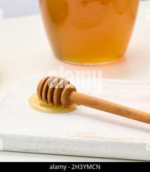 Miel dans un pot transparent en verre et bâton de bois sur une table blanche Banque D'Images