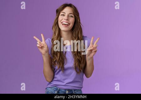 Bonne joyeuse attrayante femme exprimer positive attitude optimiste montrer la paix signes de victoire sourire largement goûtante adorable grin Banque D'Images