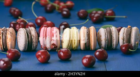 Macarons multicolores et cerises rouges mûres sur fond de bois bleu, gros plan Banque D'Images