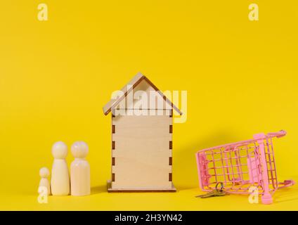 Maison en bois et chariot miniature en métal sur fond jaune.Concept d'achat immobilier Banque D'Images