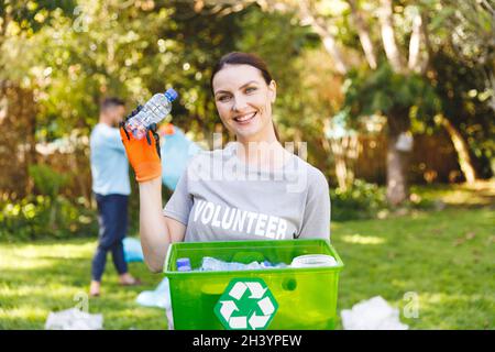Portrait d'une femme caucasienne souriante tenant une boîte de recyclage, nettoyant la campagne avec son mari Banque D'Images