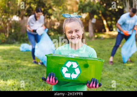 Portrait de fille caucasienne souriante tenant une boîte de recyclage, nettoyant la campagne avec les parents Banque D'Images