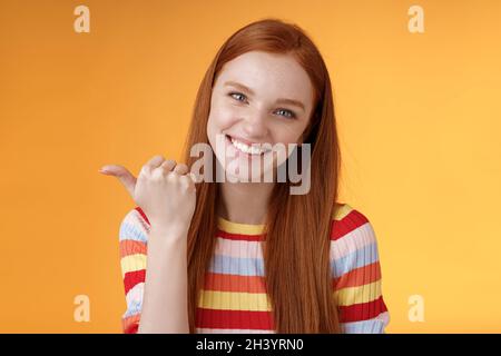 Sympathique tendre féminine genre redhead femme yeux bleus pointant vers le pouce à gauche montrant l'emplacement où trouver le produit copier l'espace volontiers Banque D'Images