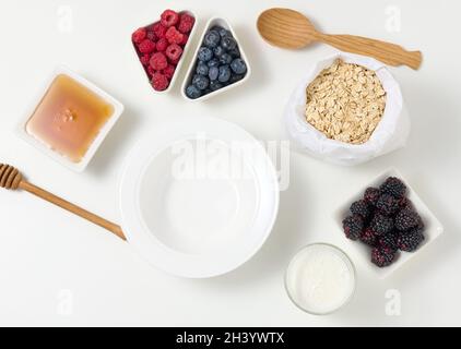 Vider la plaque blanche ronde en céramique, les flocons d'avoine et les fruits pour cuire le porridge sur une table blanche, vue du dessus Banque D'Images