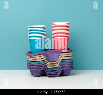 Pile de gobelets en papier multi-couleurs jetables et support sur table blanche, fond bleu Banque D'Images