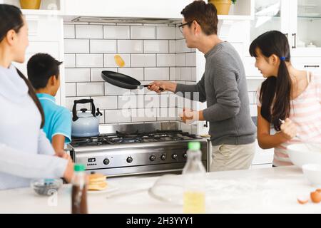 Mère, fils et fille asiatiques regardant le père lancer une crêpe pour le petit déjeuner dans la cuisine Banque D'Images
