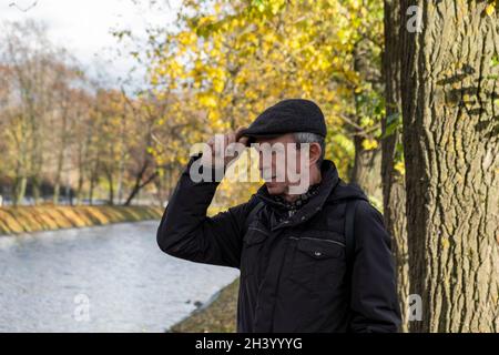 Le retraité âgé se tient en belle journée d'automne dans le parc de la ville Banque D'Images