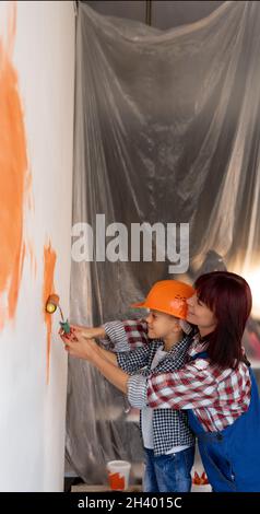Maman et son fils peignent un mur dans une nouvelle maison.Une femme enseigne à un enfant à peindre avec un rouleau lors de la réparation d'un appartement.Concept de rénovation. Banque D'Images