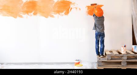 rénovation d'appartements.Vue arrière d'un garçon peint le mur avec un rouleau de peinture orange.L'enfant aide à faire des réparations.Concept de rénovation de la chambre.bannière Banque D'Images