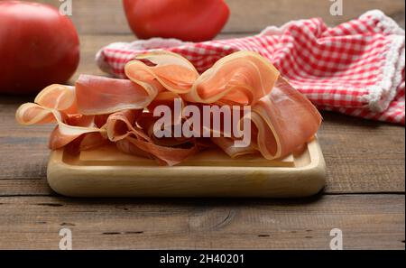 Tranches fines de prosciutto sur bois brun, fond de table en bois Banque D'Images