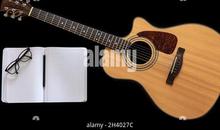 Guitare acoustique classique et carnet ouvert sur fond noir. Banque D'Images