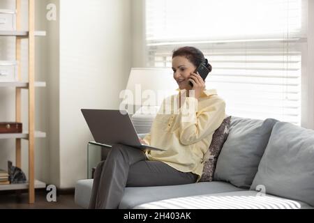 Femme d'affaires souriante d'âge moyen multitâche au bureau à domicile. Banque D'Images