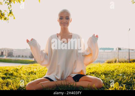 Jeune femme blonde jeunes cheveux courts en plein air faire du yoga lotus dans le parc Banque D'Images