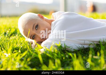 Jeune femme blonde jeunes cheveux courts plein air souriant couché sur le portrait d'herbe. Banque D'Images