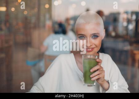 Jeune femme blonde millénial cheveux courts intérieur avec smoothie vert Banque D'Images