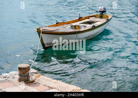 Un vieux bollard de mer en pierre sur la jetée, avec un bateau de pêche en bois attaché. Banque D'Images