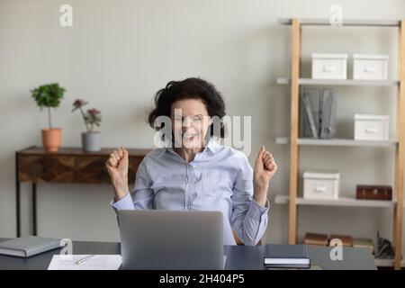 Une femme âgée des années 60 pleine de joie célèbre son succès en ligne. Banque D'Images