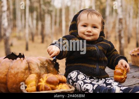 Bébé de 10 mois s'asseoir avec la citrouille et un petit pain sur une table en bois dans la forêt d'automne .Helloween concept de vacances. Banque D'Images