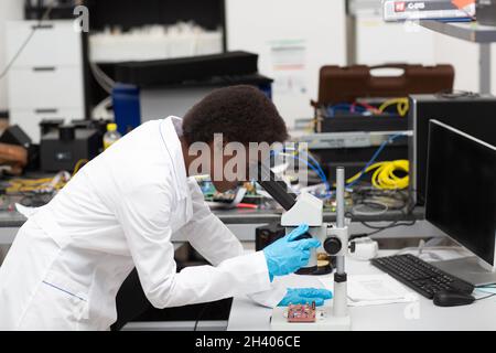 Scientifique afro-américaine femme en gants travaillant en laboratoire avec des instruments de technologie électronique et un microscope.Recherche et d Banque D'Images