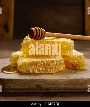 Une pile de chelines de cire avec du miel sur une planche en bois et une cuillère en bois, table brune Banque D'Images