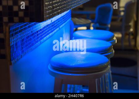 Des tabourets vides le long du bar sont éclairés par une lumière bleue Banque D'Images