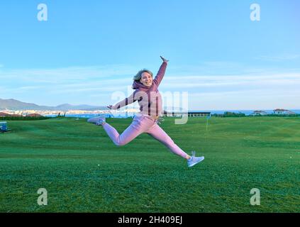 Bonne fille golfeur saut dans l'air avec les bras levés et club de golf en main après coup réussi. Banque D'Images