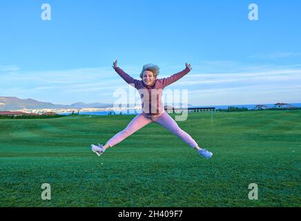 Bonne fille golfeur saut dans l'air avec les bras levés et club de golf en main après coup réussi. Banque D'Images