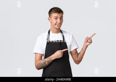 Concept des propriétaires de petites entreprises, du café-restaurant et du personnel.Un beau barista en tablier noir qui donne des conseils, des smilk et des pointées aux clients Banque D'Images