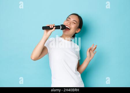 Concept de style de vie, de personnes et de loisirs. Passionnée et insouciante jolie fille asiatique chantant la chanson dans le microphone, se pencher pendant le perf Banque D'Images