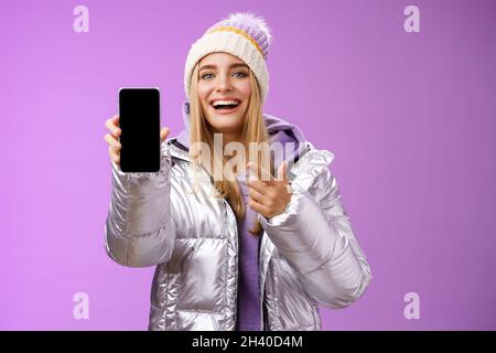 Satisfait amusé bonne apparence blonde fille suggérer prendre look smartphone afficher sourire heureux pointant téléphone mobile ravie ta Banque D'Images