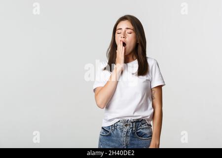 Portrait de jeune étudiante attrayante bâillant fatigué, se sentant endormi, fond blanc Banque D'Images