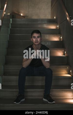 Jeune asiatique beau homme assis sur l'escalier et souriant.Chinois, génération du millénaire, mode de vie dans la grande ville, Asie moderne, pause-café Banque D'Images