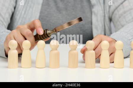 Figurines d'hommes sur une table blanche, une main femelle tient une loupe sur une. Concept de recherche d'employés dans la co Banque D'Images