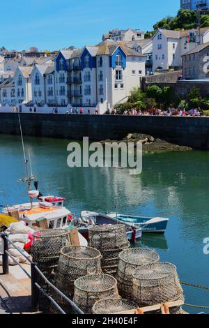 Une jolie vue sur le port de Brixham avec un bateau de pêche et des pots de homard sur le quai. Les gens qui marchent le long de la plage de Breakwater à distance. Banque D'Images