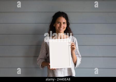 Jolie femme heureuse avec cheveux bouclés tenant un cadre photo vierge Banque D'Images