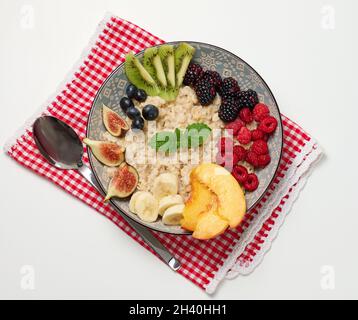 Flocons d'avoine bouillis avec fruits dans une assiette ronde sur une table blanche, petit déjeuner sain.Vue de dessus Banque D'Images