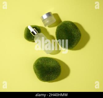 Flacons en verre blanc à usage cosmétique avec pipette sur fond vert-jaune avec des morceaux de mousse.Maquette de marque de spa de cosmétiques, haut Banque D'Images