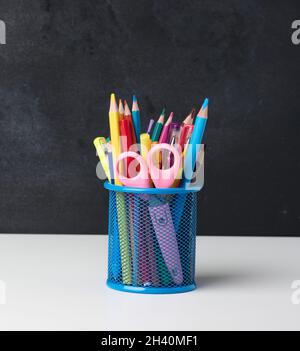 Verre métallique avec stylos, crayons, stylos-feutres et ciseaux sur le fond d'un tableau noir vide Banque D'Images