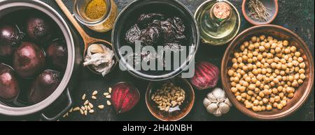 Aliments végétaliens dans des bols : betterave, pois chiches, dattes, huile, ail et pignons de pin sur une table de cuisine sombre.Ingrédients de cuisson à l'houmous. Vue du dessus.Bannière. Banque D'Images