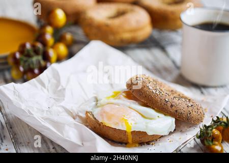 Sandwich au bagel frais et sain avec œuf frit ensoleillé, tomates cerises et café noir chaud à la vapeur.Alimentation saine.Mise au point sélective. Banque D'Images