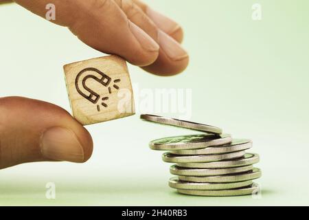 Un homme tient dans sa main un cube en bois avec une image d'un aimant près d'une pile de pièces, un concept sur le sujet de la capacité de gagner de l'argent Banque D'Images