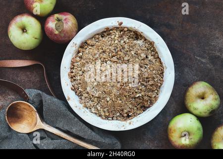 Croustillant aux pommes maison, frais et chaud ou crumble avec garniture de streusel croquante surmontée sur fond rustique avec une cuillère en bois.Vue de dessus. Banque D'Images