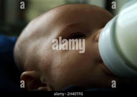 Photo portrait du bébé qui aspire le lait du biberon.Il a l'air fatigué, malheureux avec une déchirure par ses yeux. Banque D'Images